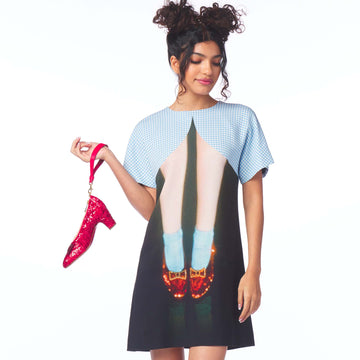 Woman wearing a dress with a graphic of red shoes and holding a pink shoe on a white background